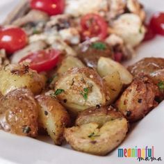 a white plate topped with potatoes, tomatoes and other food items on top of it