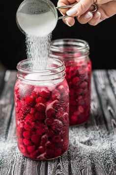 someone sprinkling sugar on raspberries in a jar