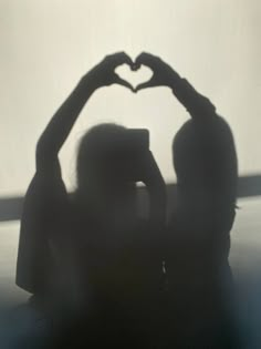 the shadow of two people making a heart shape with their hands in front of them