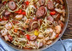 a skillet filled with shrimp, sausage and pasta on top of a wooden table