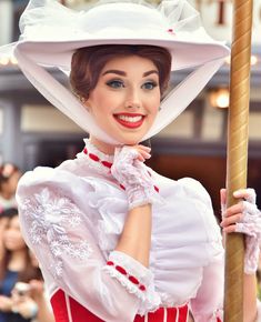 a woman in a white hat and red dress holding a pole with her right hand