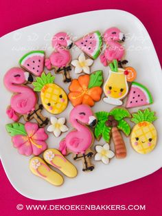 decorated cookies are arranged on a plate with pink and yellow accents, including pineapples, watermelon, flamingos, coconuts, palm trees