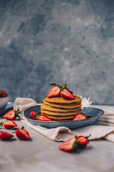 a stack of pancakes topped with strawberries on top of a blue plate next to a bowl of strawberries