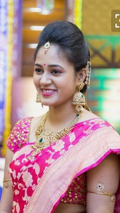 a woman in a pink and gold sari smiling at the camera with her hand on her hip