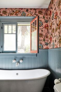 a bath tub sitting under a bathroom window next to a wall with flowers on it