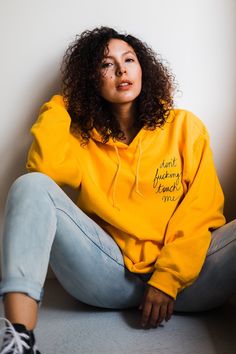 a woman sitting on the ground wearing a yellow hoodie with writing on it and black sneakers