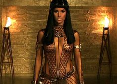 an egyptian woman with long black hair and gold body jewelry, standing in front of a golden wall