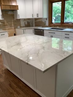 a large kitchen with white cabinets and marble counter tops on the island in front of a window