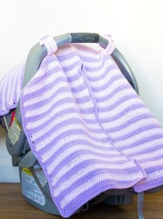 a purple and white blanket sitting on top of a car seat next to a wall