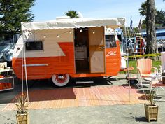 an orange and white camper parked on top of a parking lot next to trees