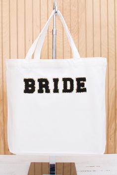 a white tote bag with the word bride on it hanging from a metal hook