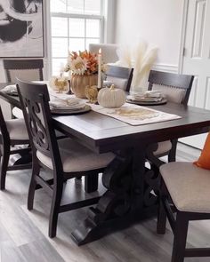 a dining room table set with place settings and fall decorations on the table, in front of a large window