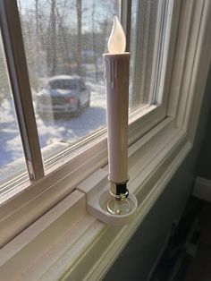 a white candle sitting on top of a window sill