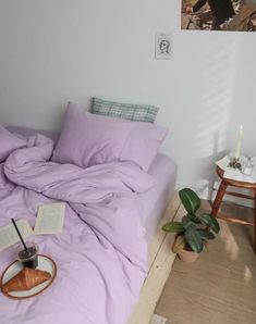 an unmade bed with purple sheets and pillows on the floor next to a plant