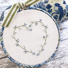 a heart - shaped embroidery on a white and blue plate with a green ribbon around it