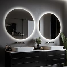 two round mirrors are above the sinks in this modern bathroom with black cabinets and white countertops