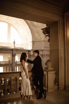 a man and woman standing next to each other in a room with large windows on the ceiling