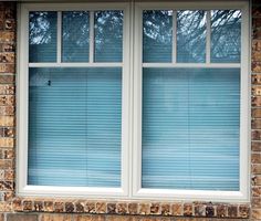 a cat sitting on the window sill in front of a brick building with blue blinds