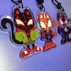 three cartoon key chains hanging on a purple surface with an image of a cat and spiderman