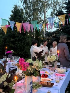 a group of people standing around a table with food and drinks on it in front of trees