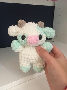 a hand holding a small white and green stuffed animal