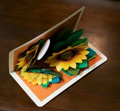 an open card with sunflowers cut out of it on a wooden table top