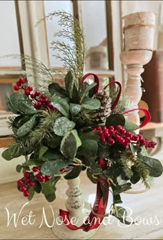 a white vase filled with greenery and red berries on top of a wooden table