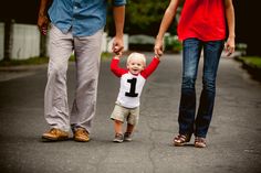 a little boy holding the hand of his mother and father as they walk down a road