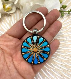 a hand holding a blue and black keychain with a flower design on it