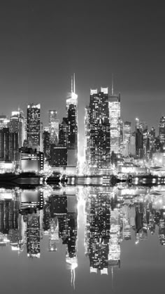 black and white photograph of the city skyline at night with reflections in the water,