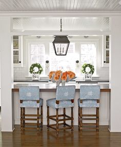 a kitchen with white walls and wooden floors has blue upholstered chairs at the bar