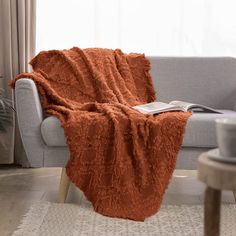 a couch with a blanket on top of it in front of a window and potted plant