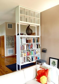 a living room filled with furniture and a book shelf next to a white couch on top of a hard wood floor