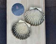 two scallop shells sitting on top of a wooden board next to a sticker