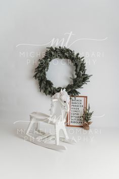 a white rocking horse next to a christmas wreath on a wall with a framed photograph