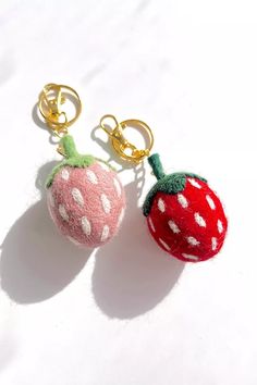 two red and white strawberry keychains sitting next to each other on a white surface