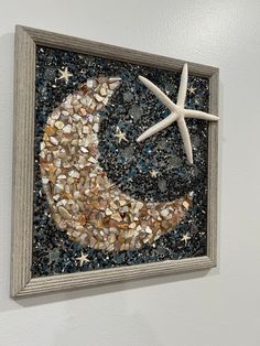 a star and moon made out of seashells on a white wall next to a wooden frame