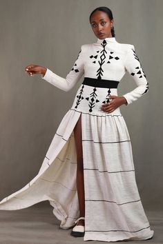 a woman in a long white dress with black and white designs on her body, posing for the camera