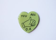 a green heart shaped pin with the words you are ok on it