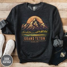 "Show off your love of Wyoming's majestic mountains with our Grand Teton National Park Sweatshirt! This vintage designed crewneck makes a great family vacation trip gift, and is all about embracing the great outdoors! It features a custom sunset design that showcases the unique shape and beauty of the Tetons which the park is known so well for! The Gildan 50/50 blend fabric has that comfy, lived-in feel, that's like a hug every time you put it on! Now you can take a bit of the Tetons with you wherever you go! Grab one now and hit the trail! * Product Highlights * Ideal for any situation, this Gildan 18000 heavy blend crewneck sweatshirt is pure comfort. Made from an extremely soft 50/50 polyester and cotton blend, this combination helps keep you warm and comfortable. The collar features a Winter Hiking Crew Neck Top, Relaxed Fit Crew Neck Tops For Hiking, Outdoor Graphic Print Crew Neck Sweatshirt, Crew Neck Letter Print Hiking Top, Graphic Print Crew Neck Sweatshirt For Outdoor, Graphic Print Crew Neck Tops For Outdoor Activities, Graphic Print Crew Tops, Relaxed Fit Graphic Print Sweatshirt For Outdoor Activities, Relaxed Fit Crew Neck Sweatshirt For Hiking