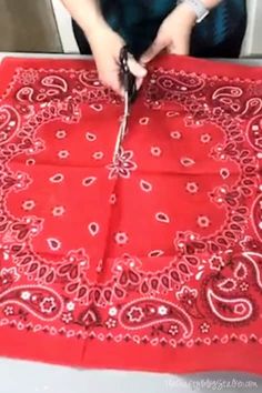 a woman is cutting fabric with scissors on a red table cloth that has been sewn