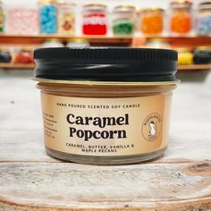 a jar of caramel popcorn sitting on top of a wooden table next to shelves