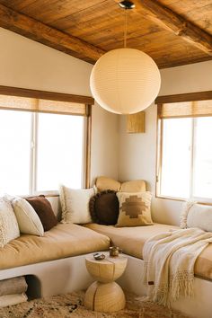 a living room filled with lots of furniture and pillows on top of a couch next to two windows