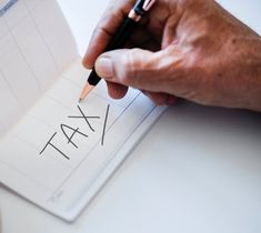 a person writing on a piece of paper with a pencil in their hand and the word tax written on it