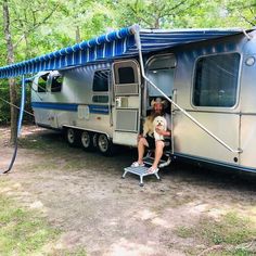 a woman and her dog are sitting in the doorway of an rv with awnings