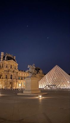 the large building is lit up at night with lights on it's sides and pyramids in the background