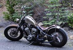 a motorcycle parked on the side of a road next to some bushes and trees in the background