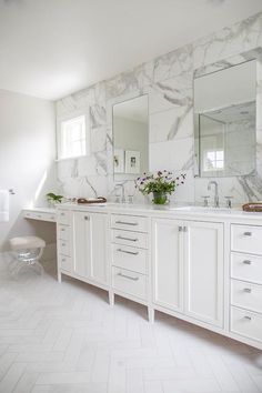 a white bathroom with marble counter tops and double vanity sinks, along with two mirrors on the wall