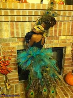 a woman in a peacock costume standing next to a fire place with feathers on it