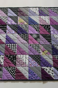 a patchwork quilt is hanging on the wall in front of a white wall with black and purple designs